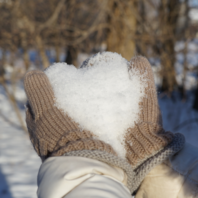 Mittens holding snow in the shape of a heart